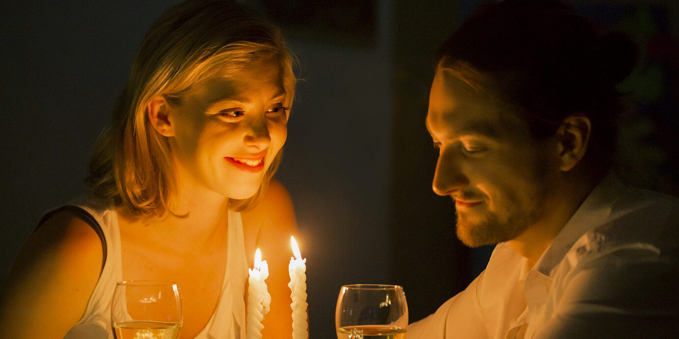 Sharing a smile A woman listens intently as she gazes across at her partner as they sit at a candle lit table and drink white wine.