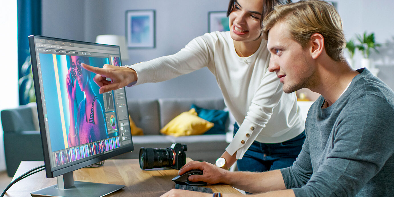 Male and Female Professional Editors Talk while Working in Photo Editing App / Software on a Personal Computer. Photo Editors Retouching Photos of a Beautiful Girl. Mock-up Software Design. Female Points at the Screen.