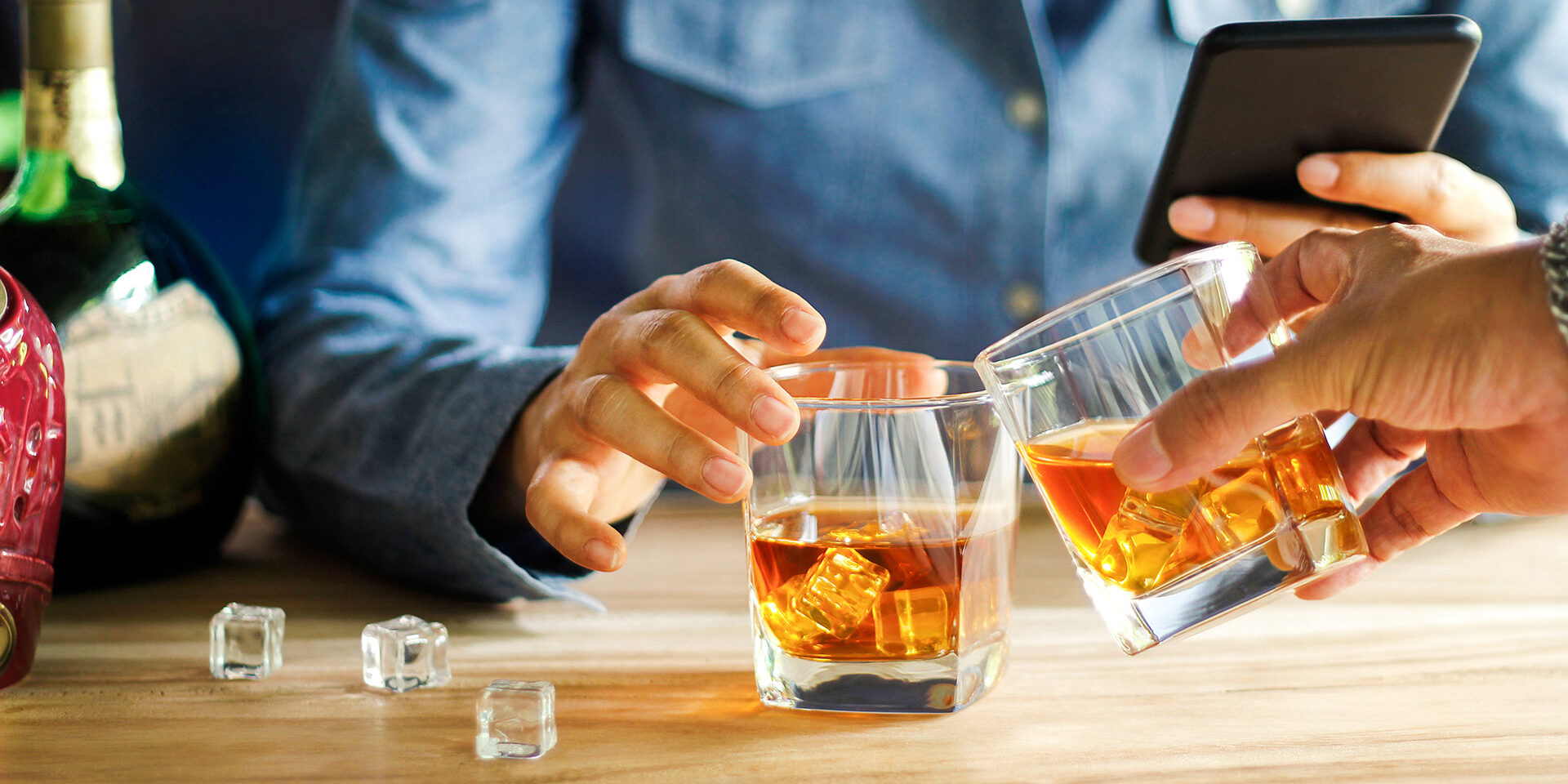 Close-up of two men clink glasses of whiskey drink alcoholic beverage together while at bar counter in the pub