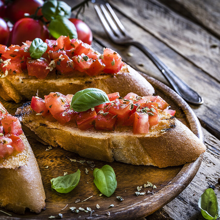 Italian food: homemade bruschetta ready to eat shot on rustic wooden table. Olive oil, tomatoes and peppercorns complete the composition. Predominant colors are red and brown. XXXL 42Mp studio photo taken with Sony A7rii and Sony FE 90mm f2.8 macro G OSS lens