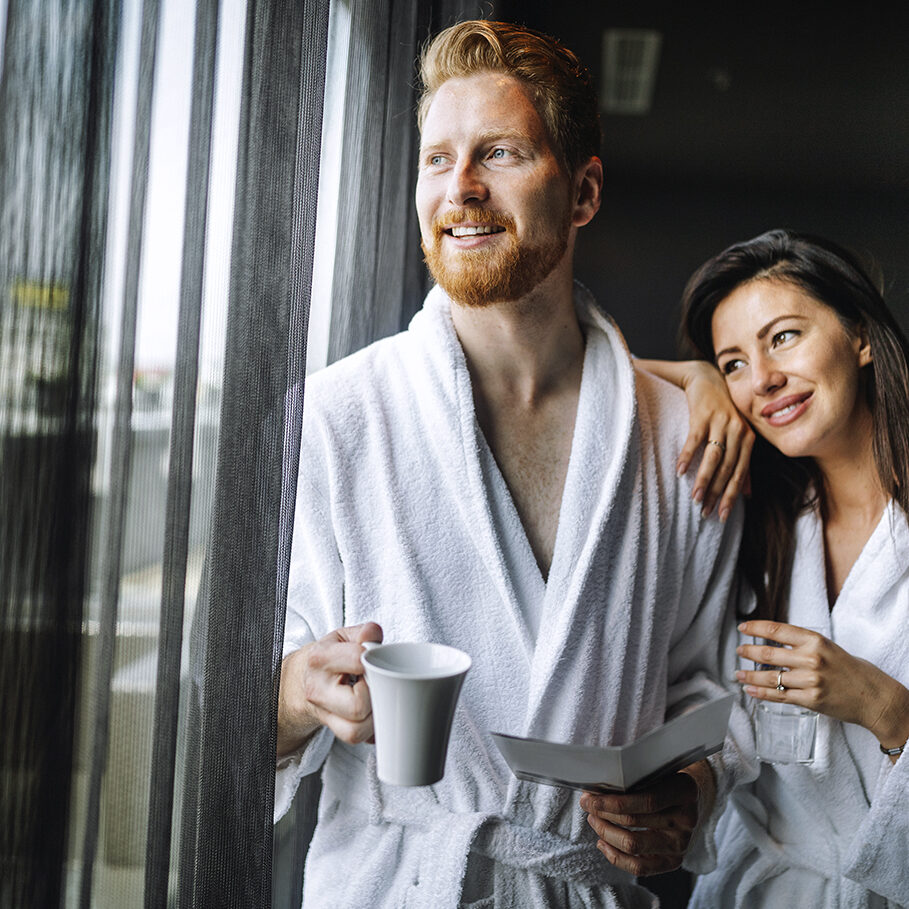 Happy young couple in white bathrobes drinking coffee together at morning