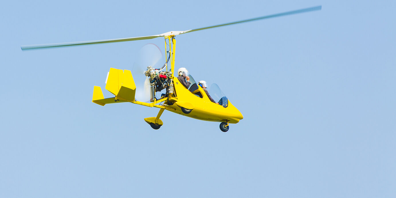 Autogiro flying against clear blue sky.
