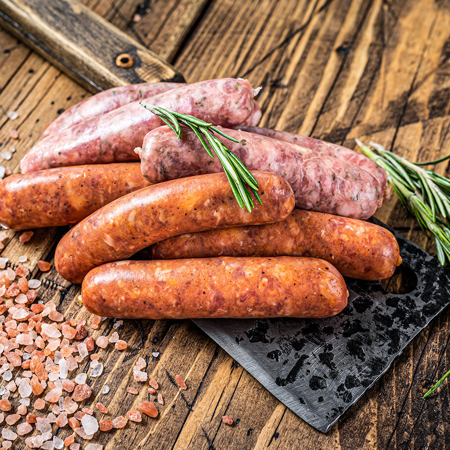 Assorted Raw pork and beef sausages on a butcher meat cleaver. wooden background. Top View.