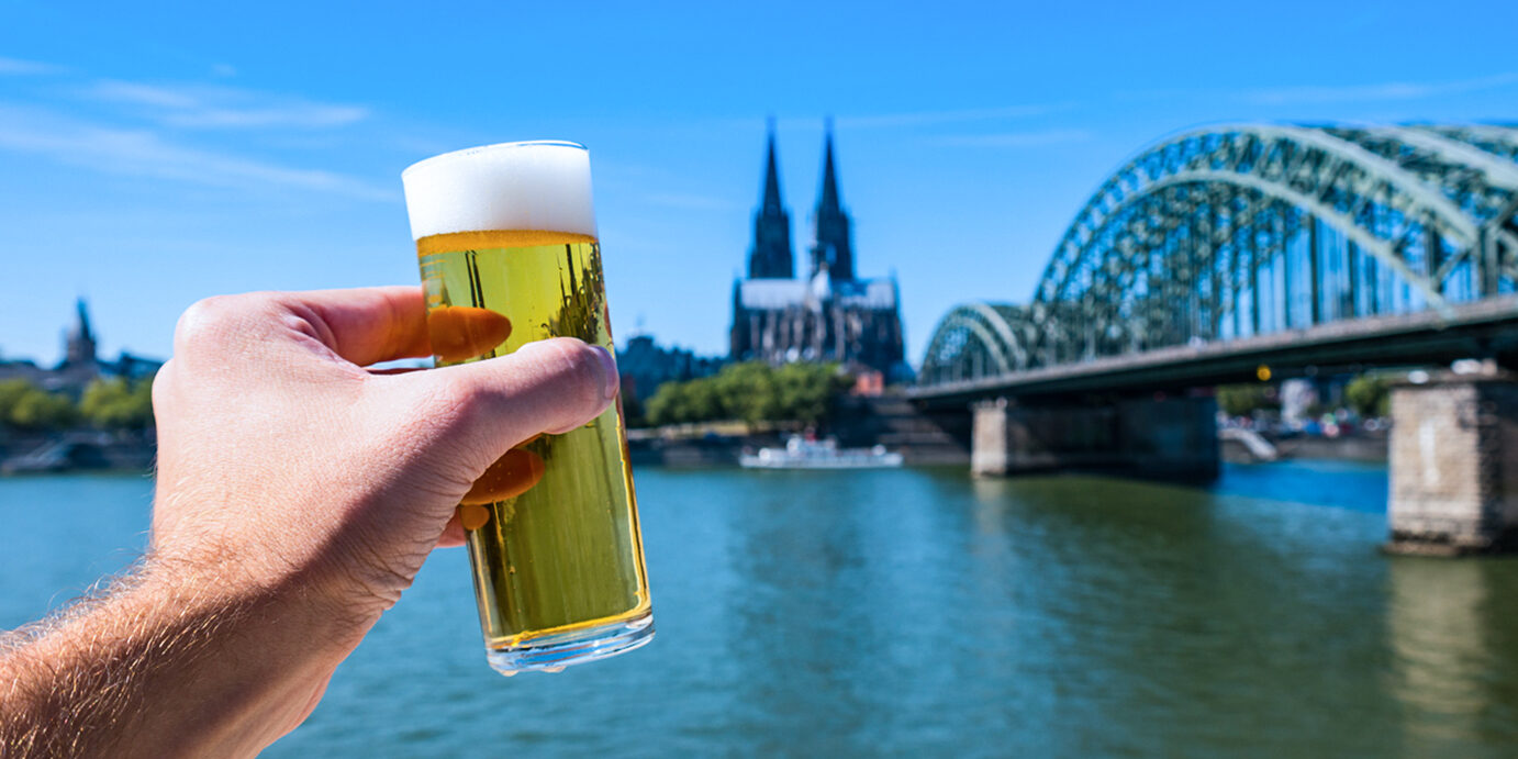 German beer (Kölsch) at Cologne at the rhine river Germany young man holding a beer glass at the rhine river with hohenzollern bridge and cathedral in cologne. ideal for websites and magazines layouts