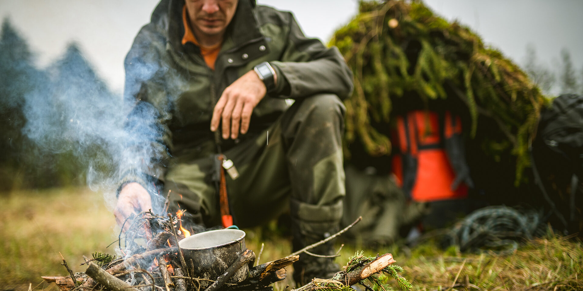 Hiker making tea with leaves on campfire in forest.