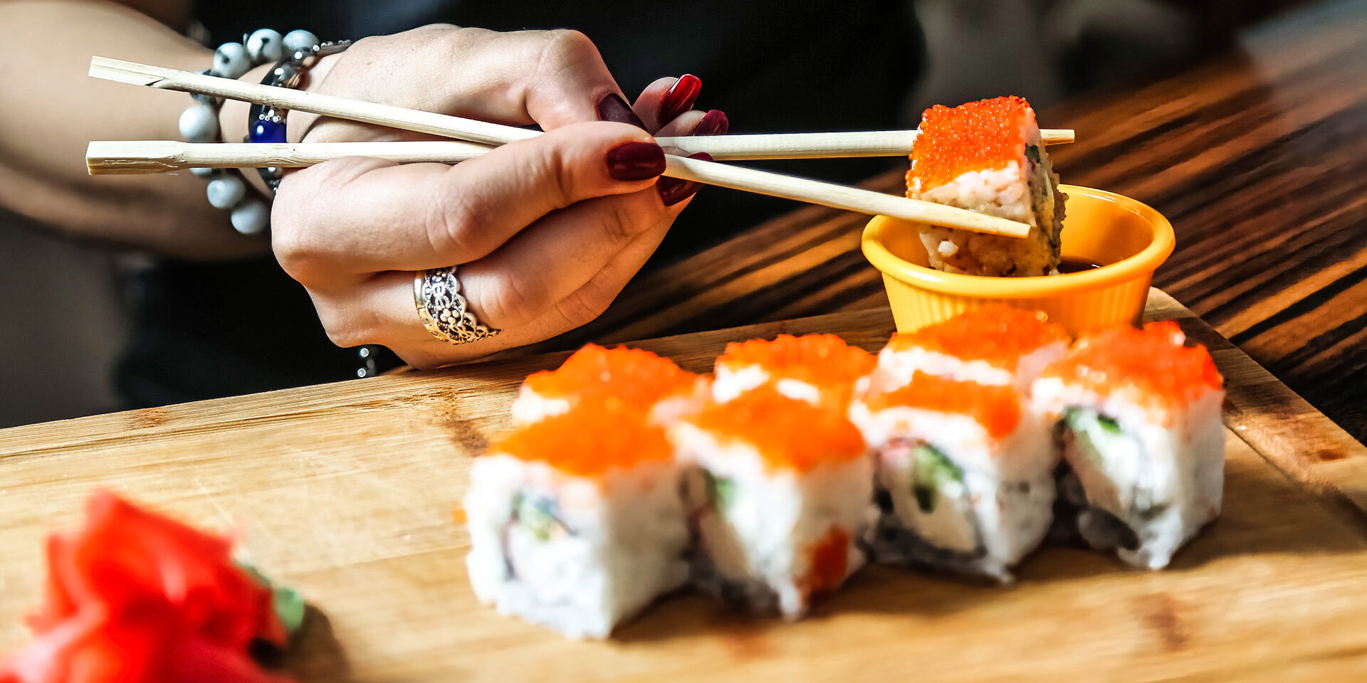 Woman Holding Chopsticks Over a Plate of Sushi A woman delicately holds a pair of chopsticks over a plate filled with fresh sushi rolls.