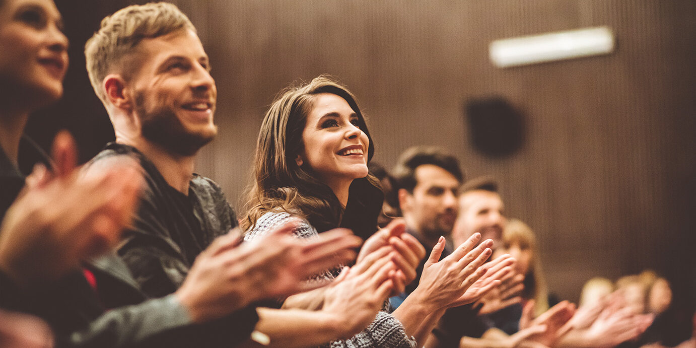 Happy people applauding in the theater Group of smiling people clapping hands in the theater, focus on audience. Dark tone.