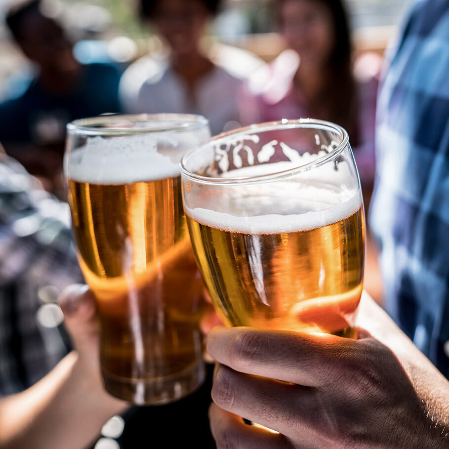 Close up of a customers at a bar holding a beer and making a toast with people having fun at the background