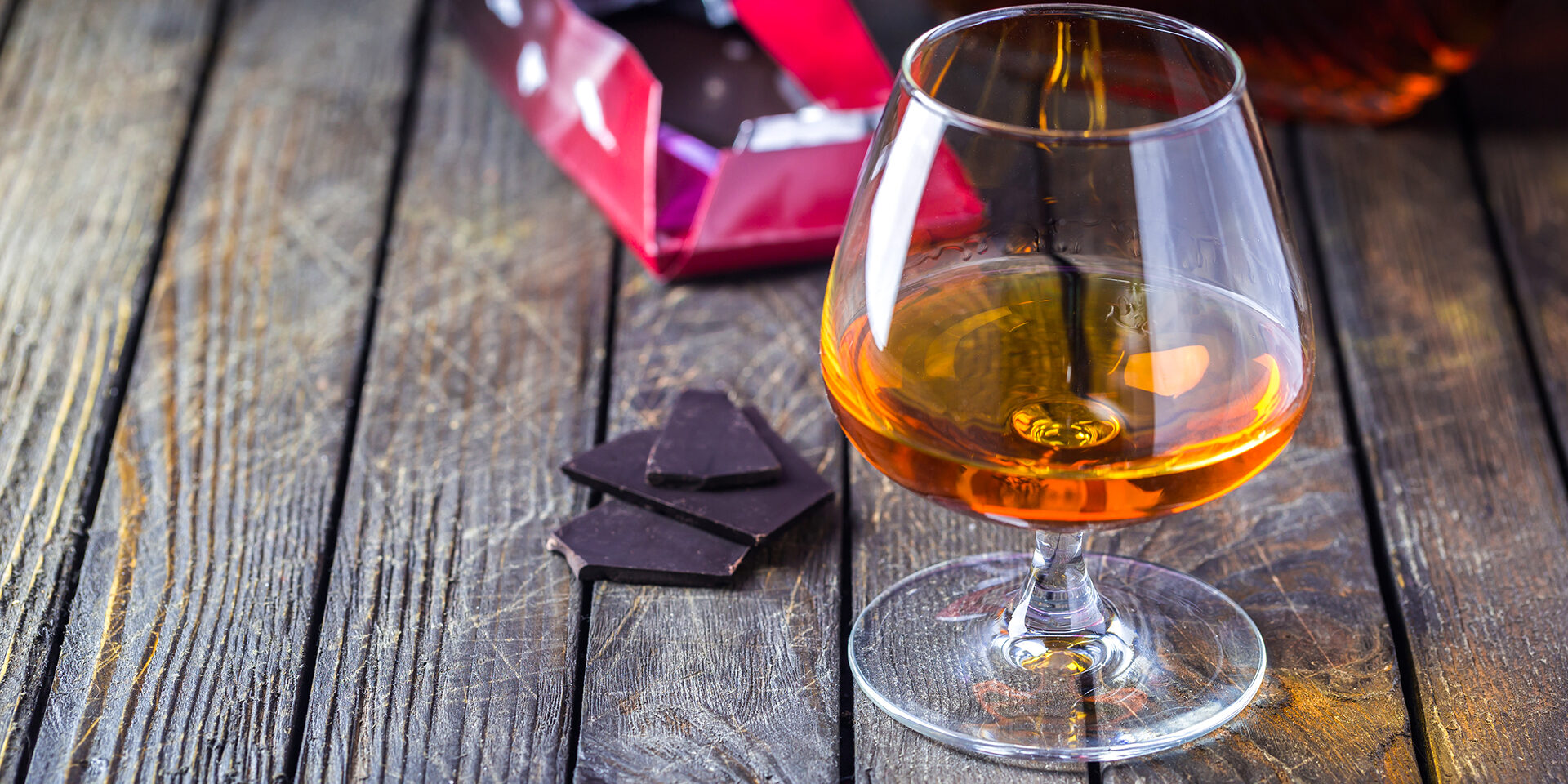 Glasse of brandy or cognac and bottle with chocolate on dark background.