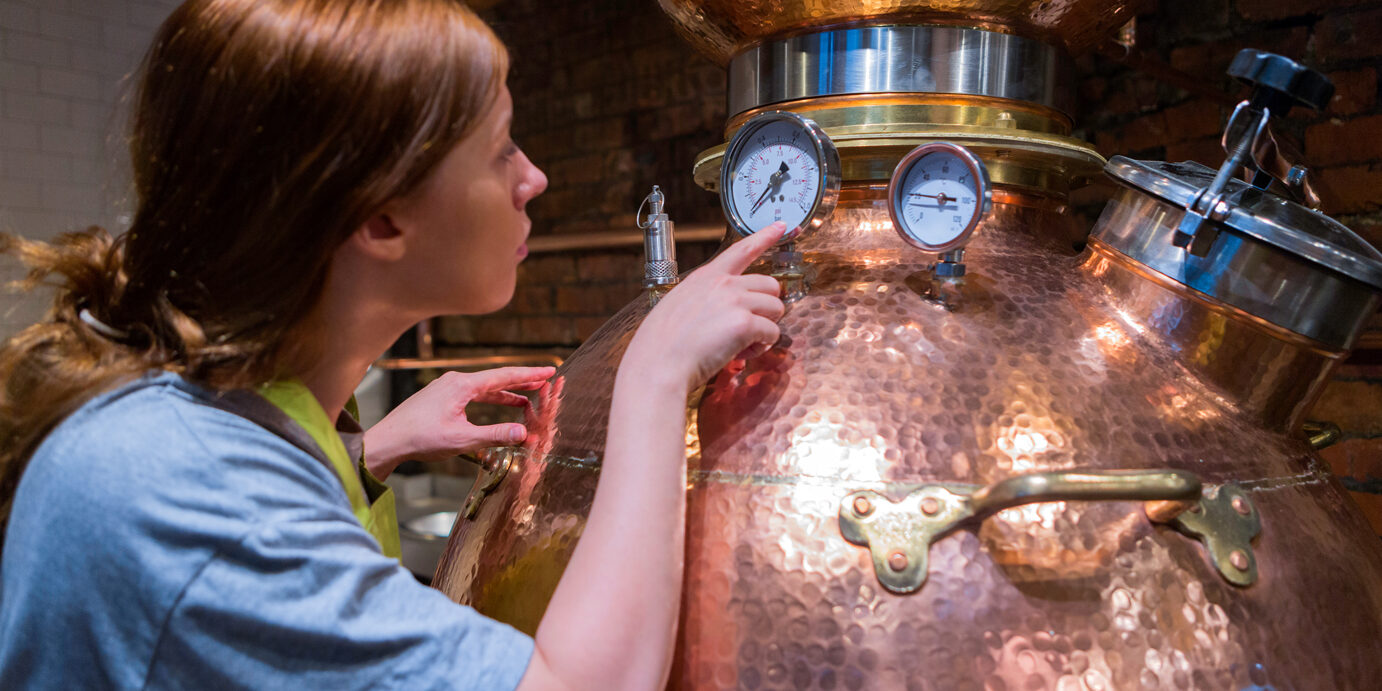 A female worker is checking the dials and temperature on the copper distillery boiler. It is used to produce Gin and Whiskey.