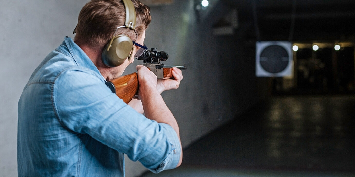 Handsome serious man looking at the target Hitting the bulls eye. Handsome confident serious man holding the rifle and looking into the target while trying to hit the bulls eye
