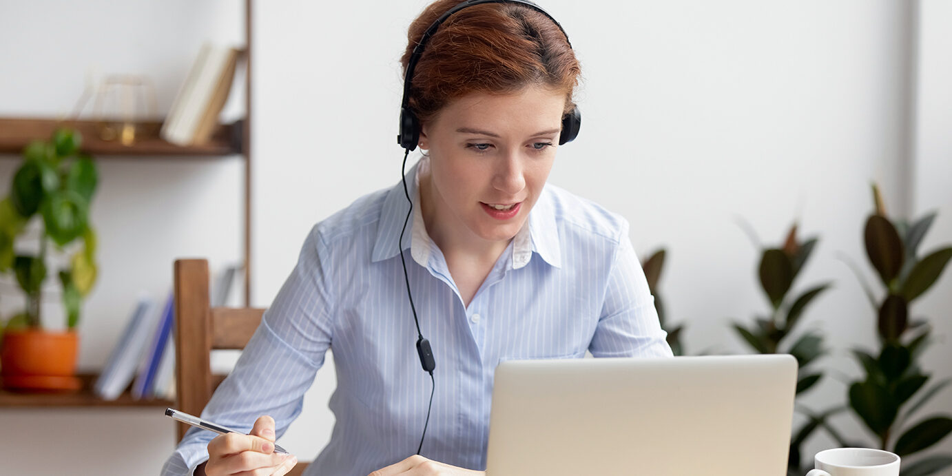 Businesswoman wearing headphones watching video webinar making conference online call writing notes talking on skype, focused woman study online looking at laptop listening translating lecture course