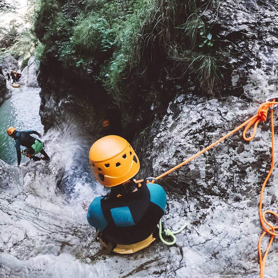 Woman canyoning in Slovenia, woman wearing neoprene and safety gear rappelling in the canyon.