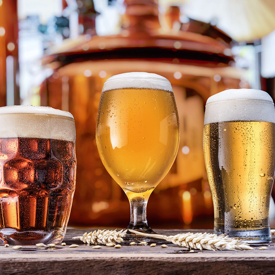 Beer glasses  on wooden table and copper brewing cask at the background. Craft brewery.