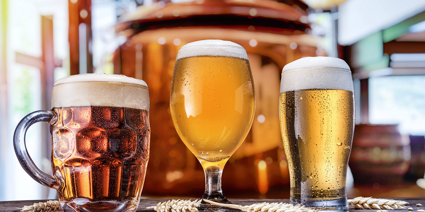 Beer glasses on wooden table and copper brewing cask at the background. Craft brewery. Beer glasses on wooden table and copper brewing cask at the background. Craft brewery.