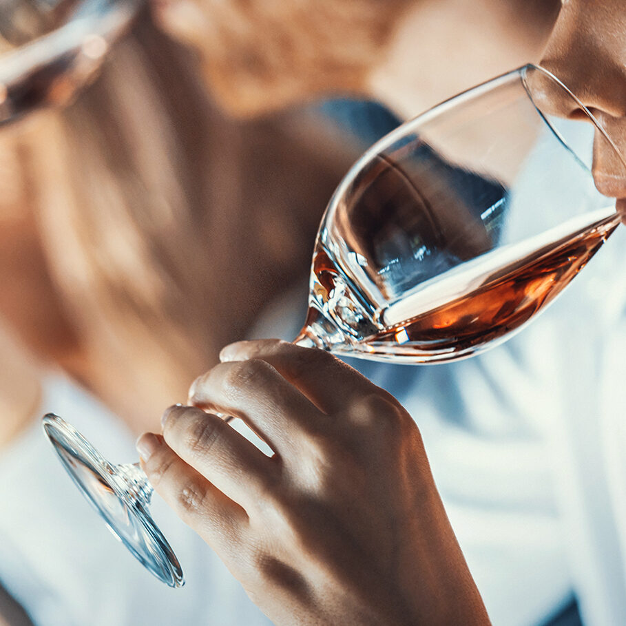 Closeup side view of group of unrecognizable adults tasting different wines at a local winery. They are using wine charts and writing down their impressions. Focus on the closest person to the camera. Tilt shot.