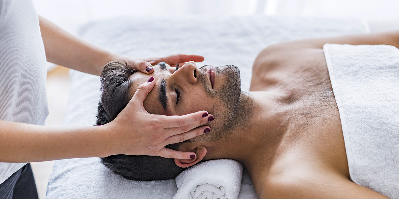 Young man relaxed in spa. Male beauty - man receiving facial massage at luxury spa. Young man relaxed in spa. Closeup of a man having head massage. Man getting a face massage. Close-up of a man receiving facial massage at the spa"r"n