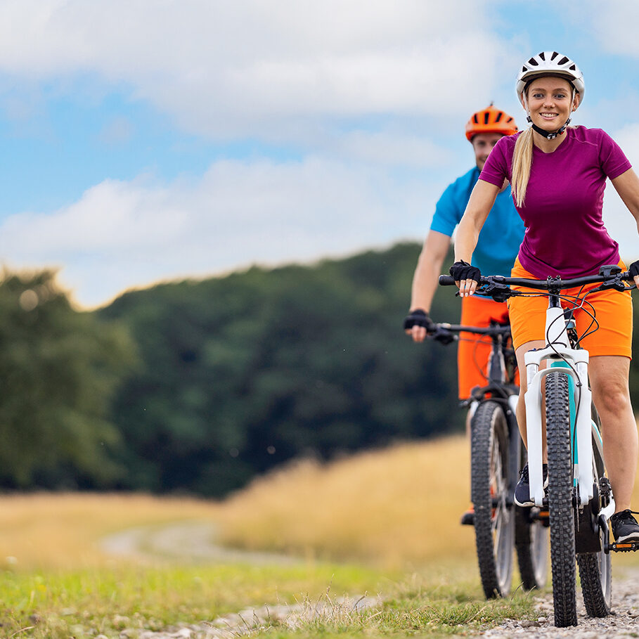 happy smiling couple cycling down gravel road in rural landscape with elctric mountain bikes in summer, focus on woman, place for text