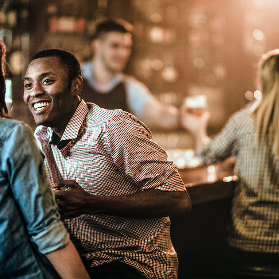 Happy black man enjoying in a talk with his girlfriend while being in a bar. There are people in the background.