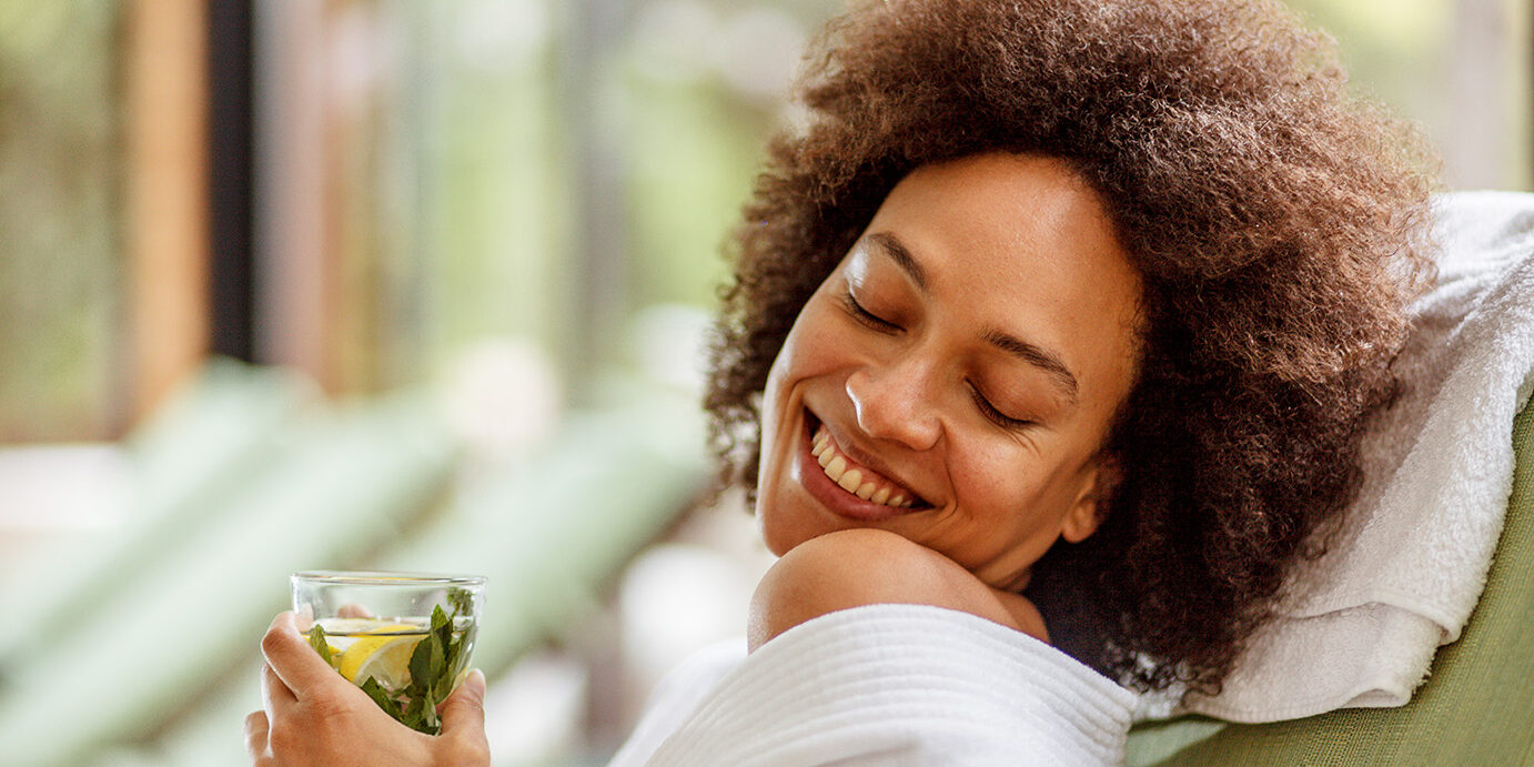 Happy times at the spa Smiling young woman relaxing in a cozy bathrobe while enjoying a refreshing herbal tea on her weekend getaway at the wellness resort.