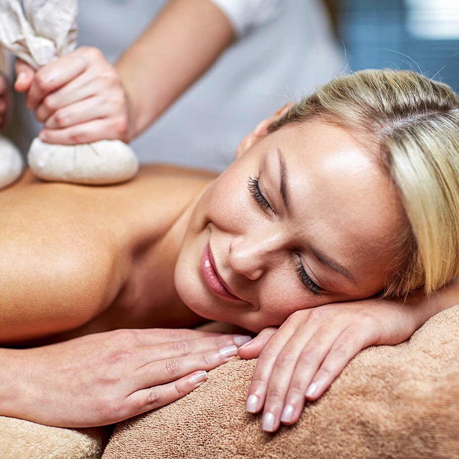 people, beauty, spa, healthy lifestyle and relaxation concept - close up of beautiful young woman lying and having herbal bag massage in spa