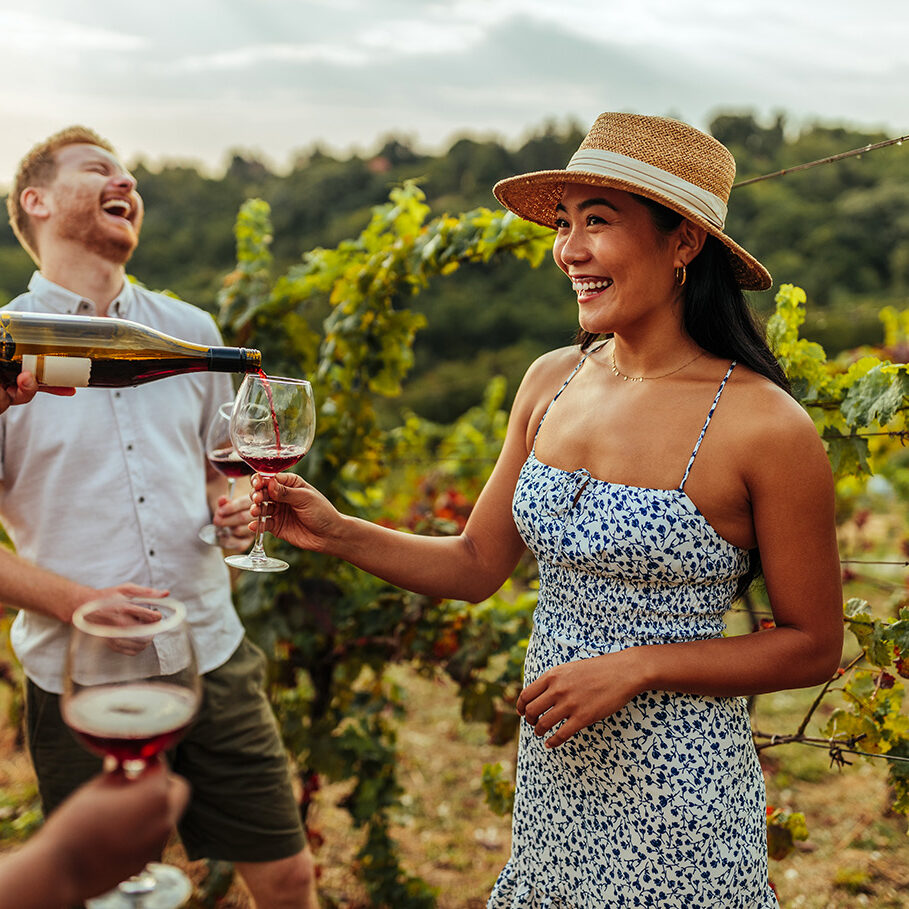 Man pouring glass of wine to his female asian friend in vineyard