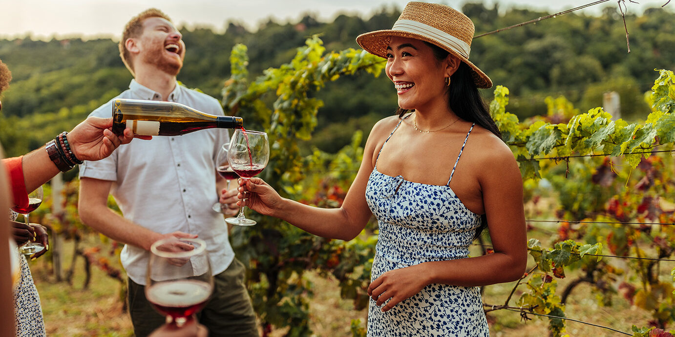 Wine tasting with friends in vineyard Man pouring glass of wine to his female asian friend in vineyard