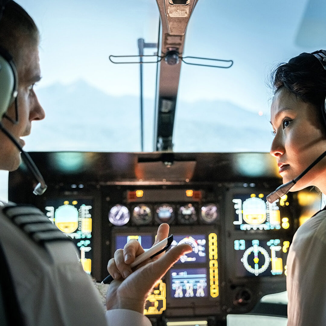 Female trainee pilot listening to instructor during a flight simulation training. Woman learning to fly helicopter with instructor inside a flight simulator.