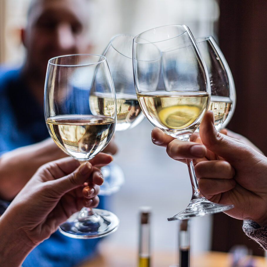 Friends toasting each other with white wine, smiling, sitting in restaurant