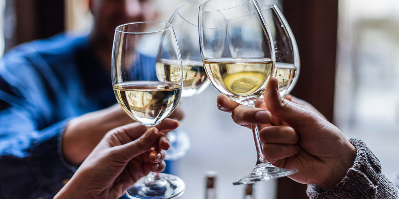 Group of friends toasting with wine glasses Friends toasting each other with white wine, smiling, sitting in restaurant