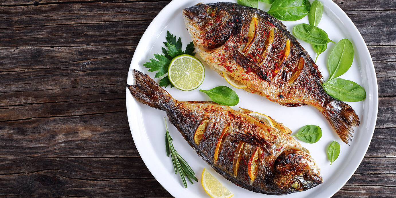 roasted sea bream fish with lemon slices delicious roasted dorado or sea bream fish with lemon and orange slices, spices, fresh parsley and spinach on white platter on old dark wooden table view from above