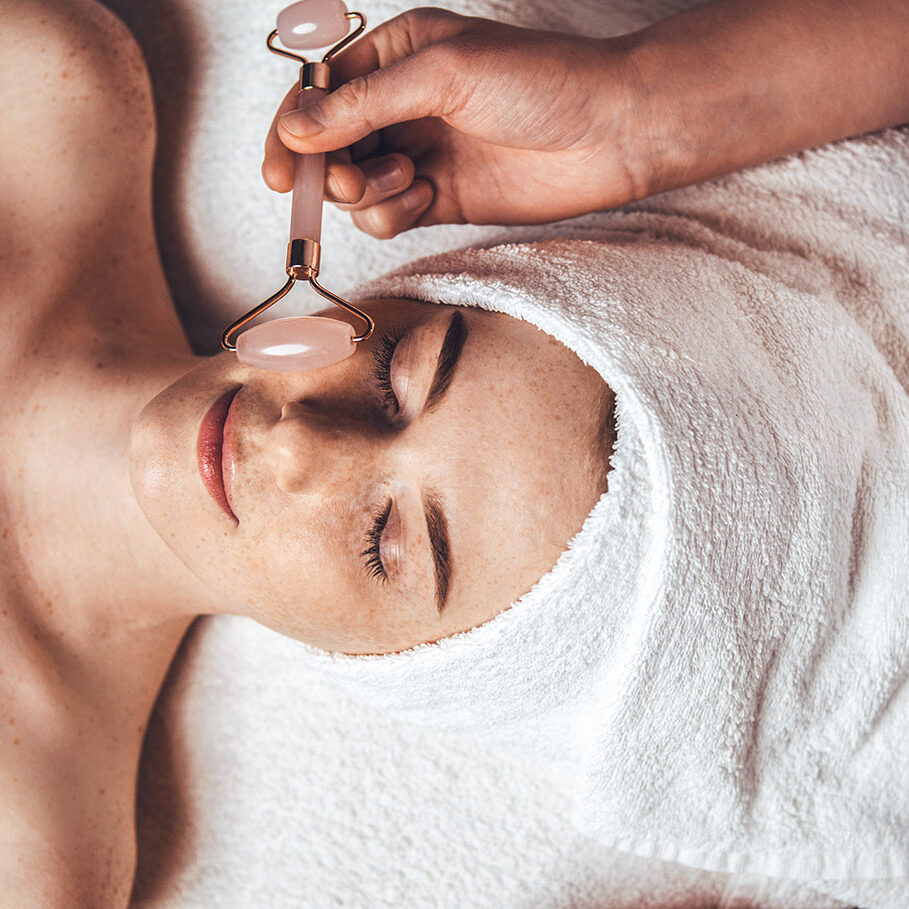 Close up portrait of beautician's hand massaging patient's face with jade roller at spa salon. Beauty woman face skin care. Body care, spa.