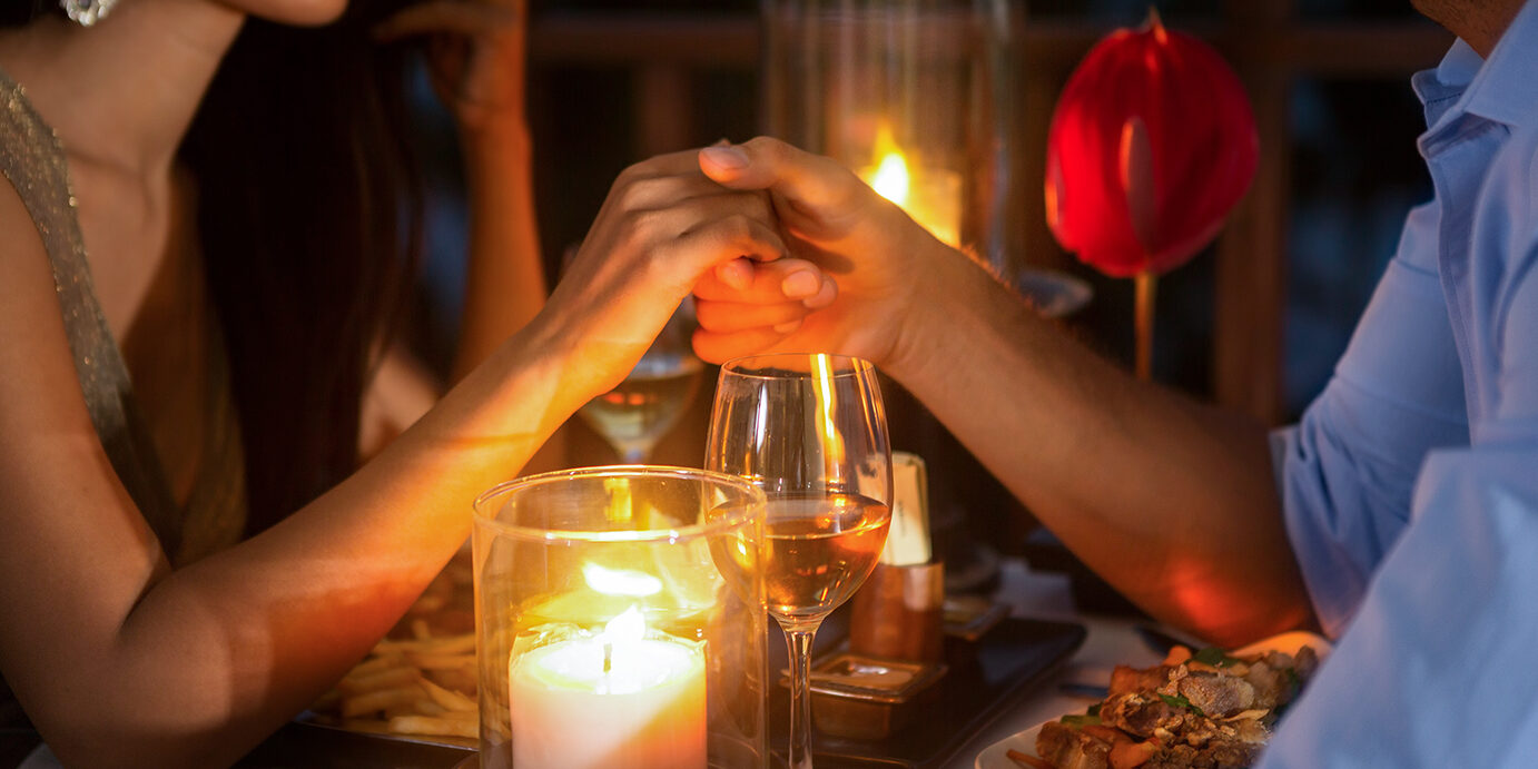 Romantic couple holding hands together over candlelight during romantic dinner