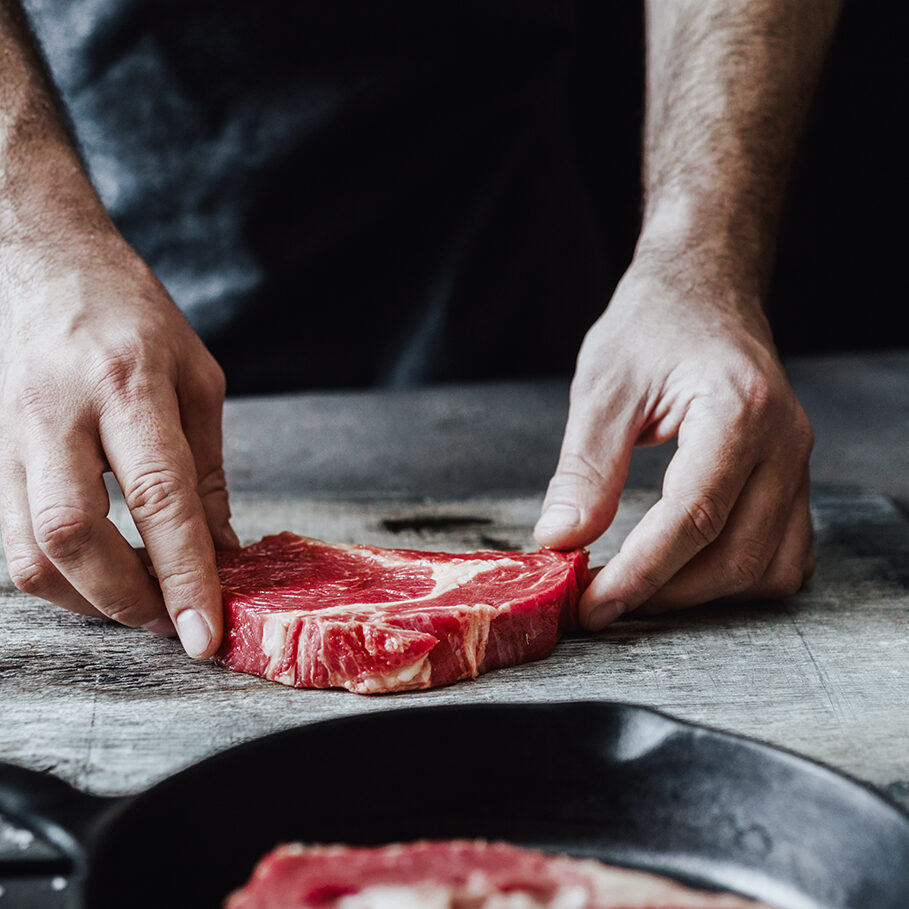 Man preparing beef steak on wooden table.