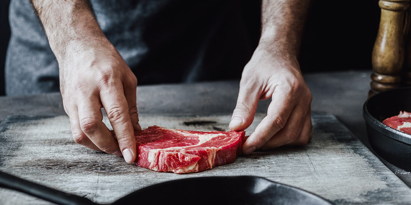 Man preparing beef steak on wooden table Man preparing beef steak on wooden table.