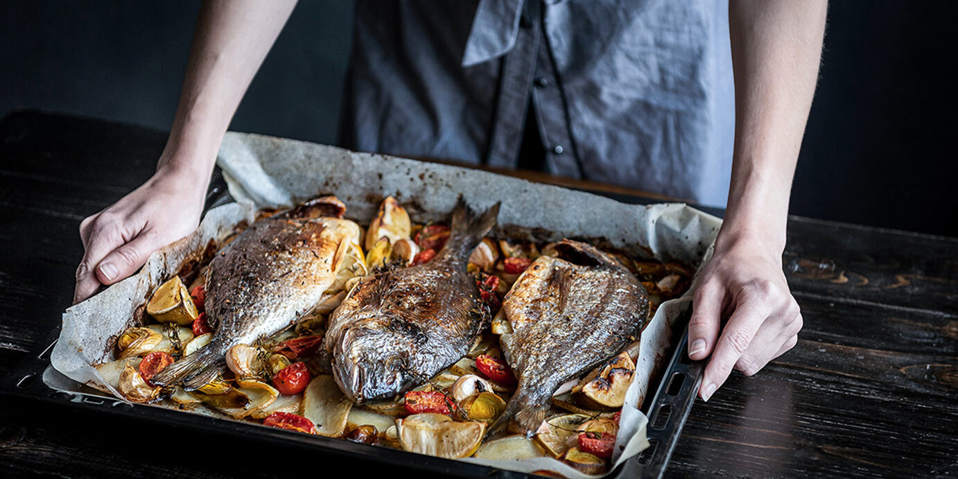 baked fish fish for dinner. in female hands baked fish on a baking sheet.