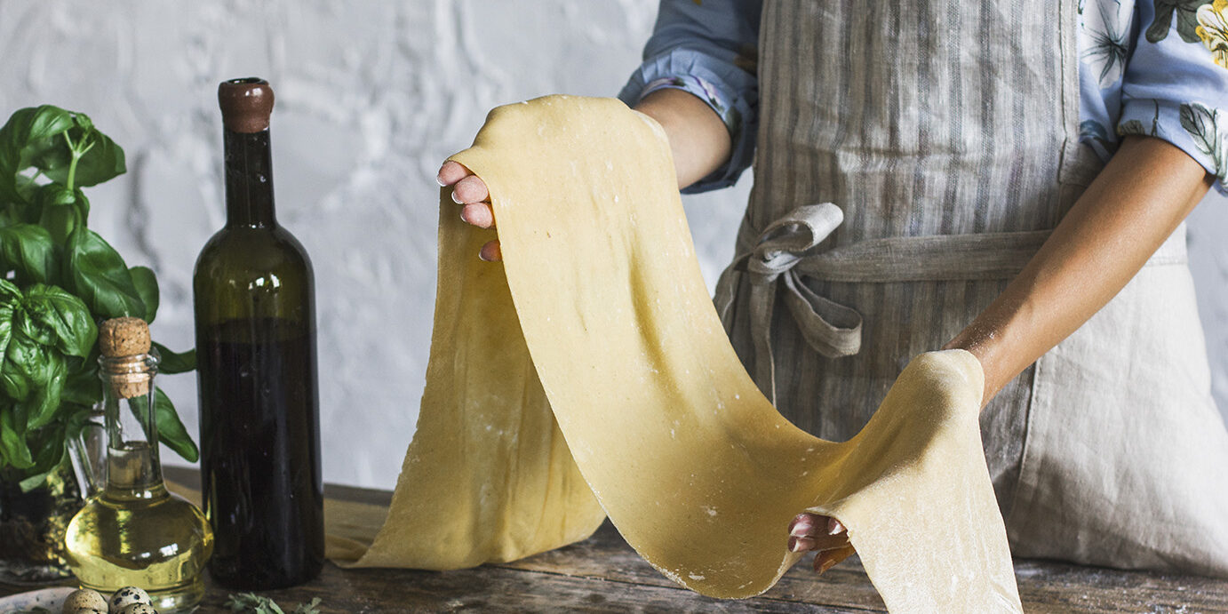 Young woman in apron holding the dough for homemade pasta at rustic kitchen Young woman in apron holding a dough for homemade pasta at rustic kitchen