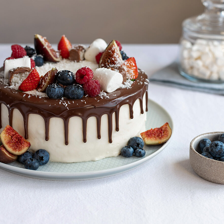 closeup of berry cake decorated with marshmallows and chocolate ganache on white tablecloth. Birthday, Mothers Day concept. Modern dessert