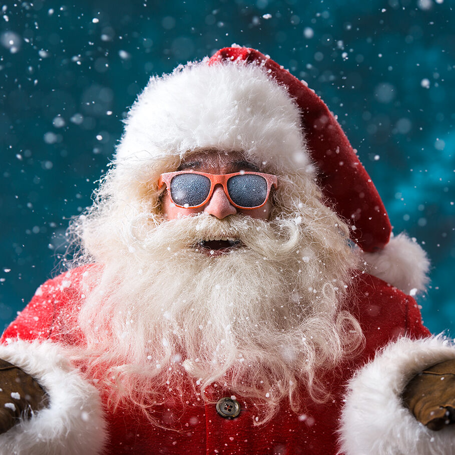 Santa Claus wearing sunglasses dancing outdoors at North Pole in snowfall. He is celebrating Christmas after hard work