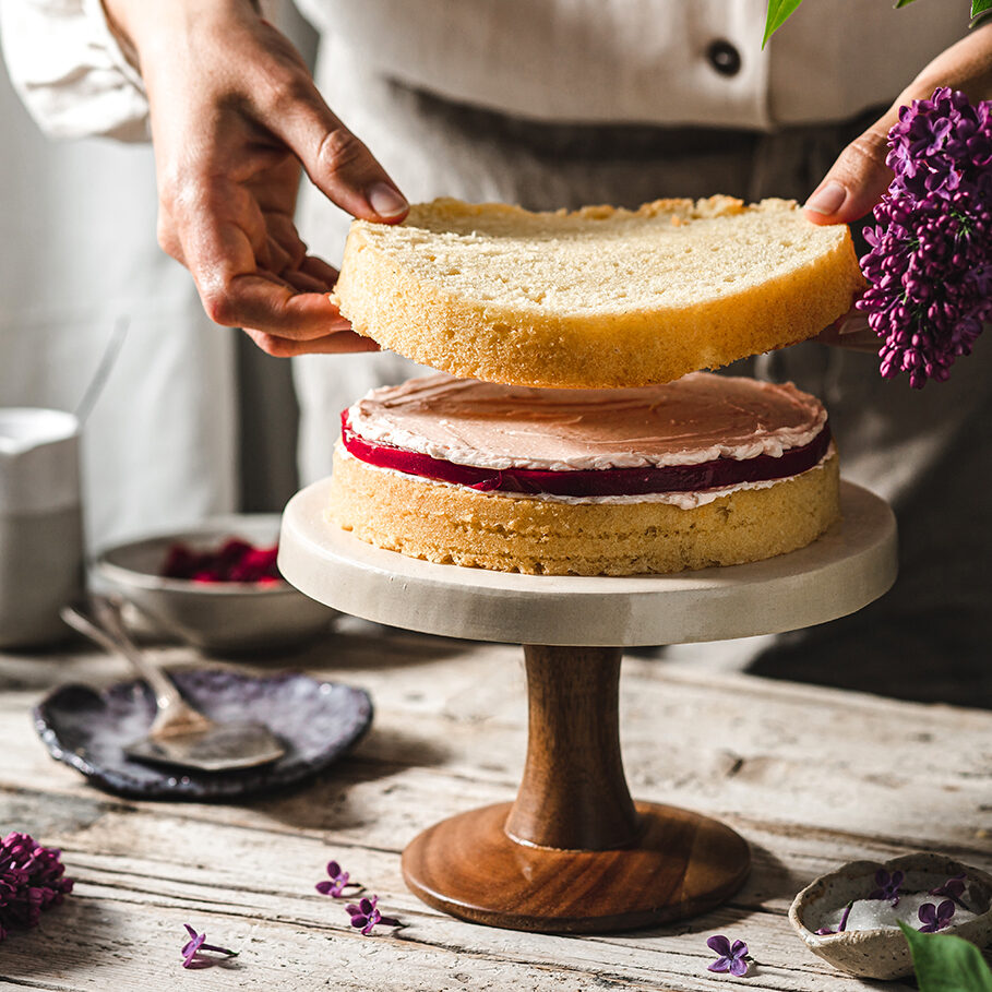 Close-up of female chef preparing cake. Woman making a layer cake with ingredients on table.