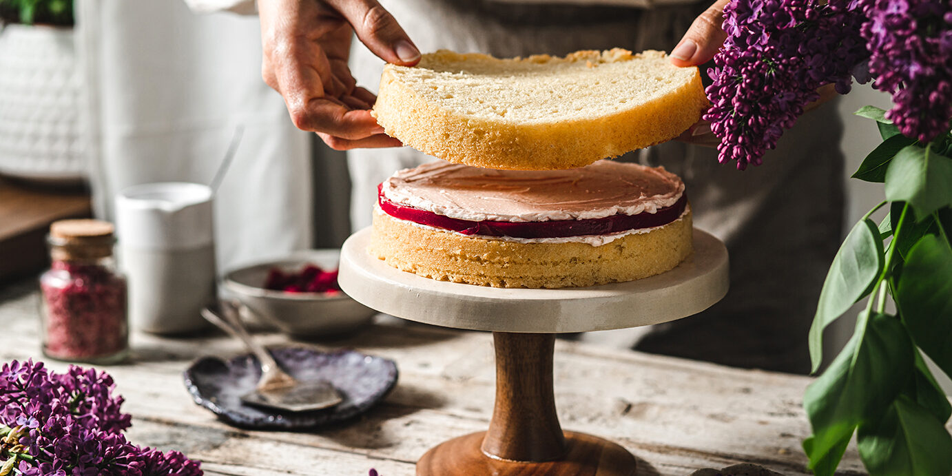 Close-up of female chef preparing cake. Woman making a layer cake with ingredients on table.