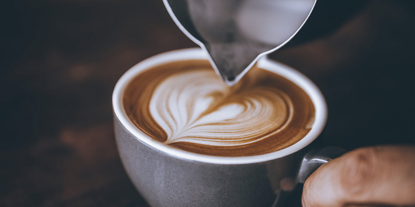 Barista making pouring stream milk with coffee latte art pattern heart shape.
