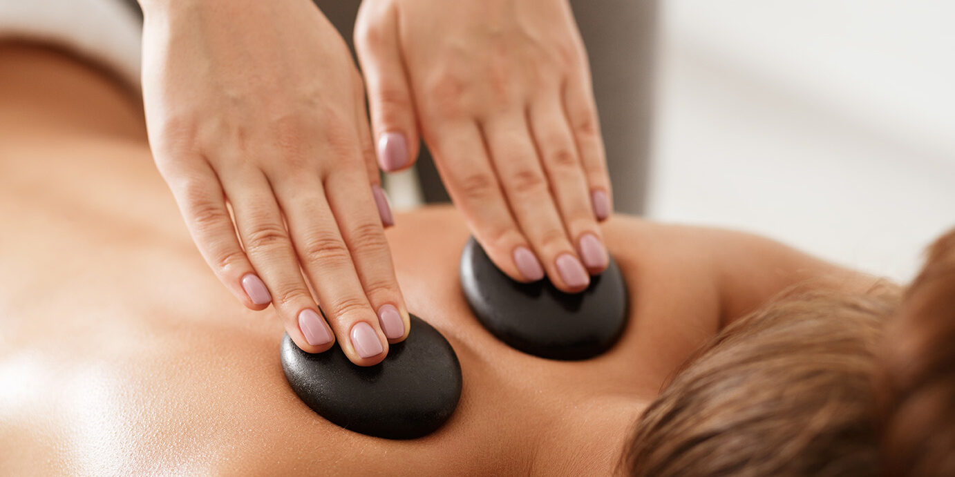 Relaxed woman getting stones shoulder massage in spa Relaxed woman getting hot stones massage, masseur placing stones on back, closeup