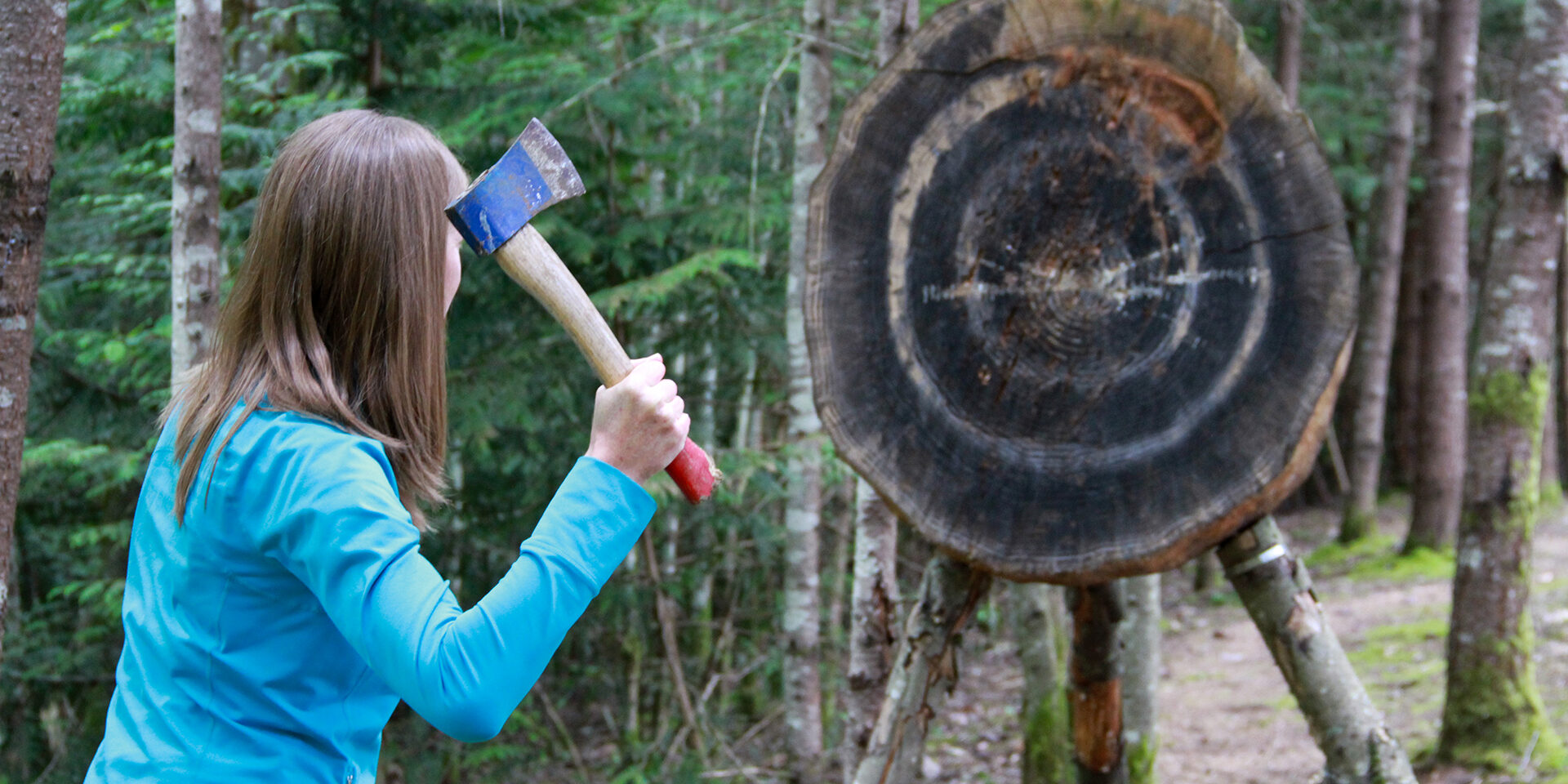 Lady Hatchet Thrower A young woman is preparing to throw a hatchet at a large target in the forest.