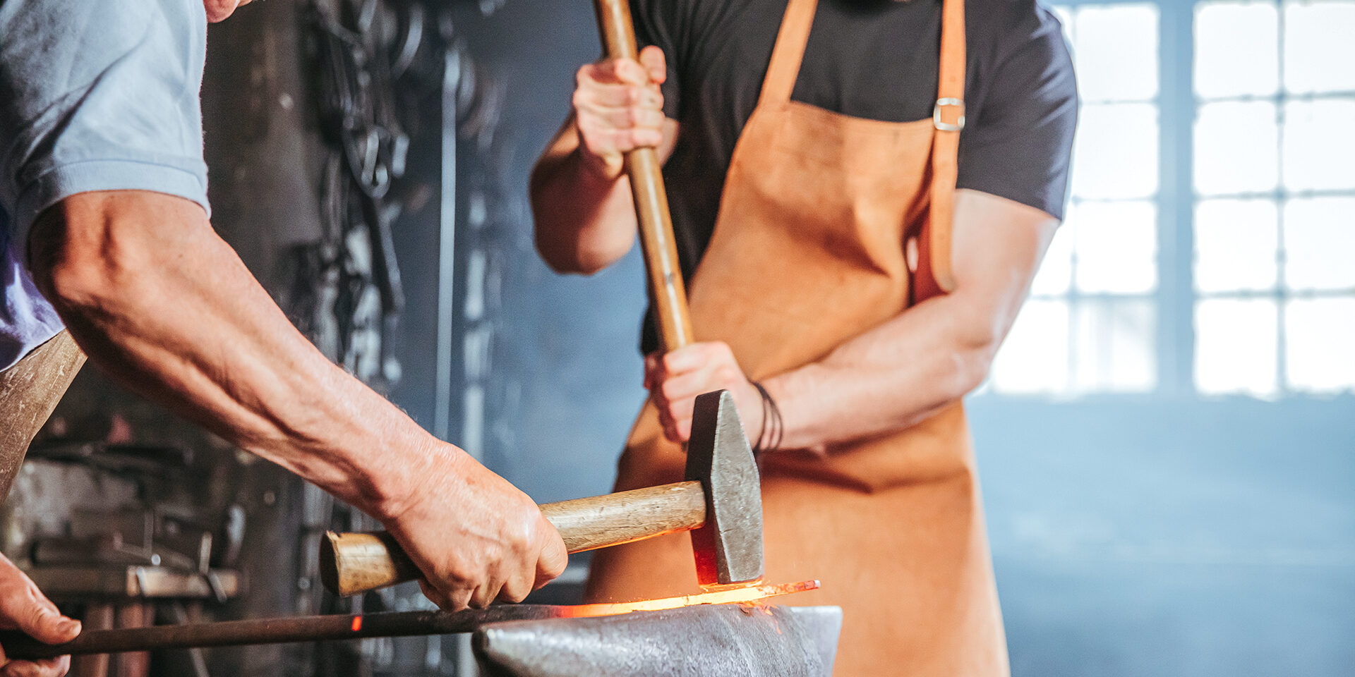 Two blacksmith hitting hammer on hot metal piece Two blacksmith hitting hammer on hot metal piece at workshop