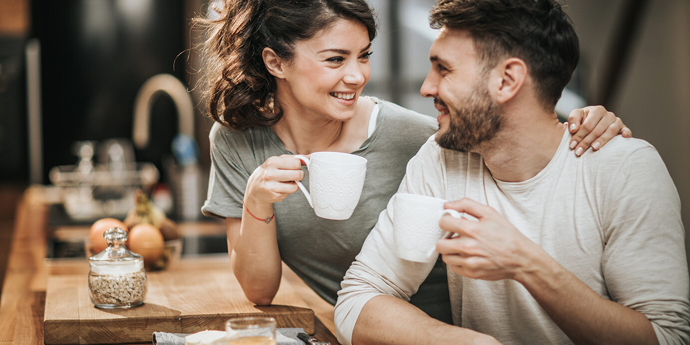 Young happy couple talking while drinking coffee in the morning. Focus is on woman.