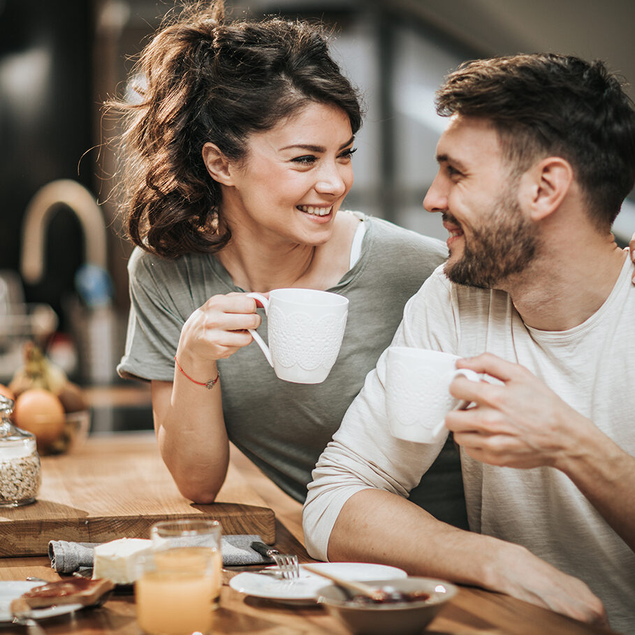 Young happy couple talking while drinking coffee in the morning. Focus is on woman.