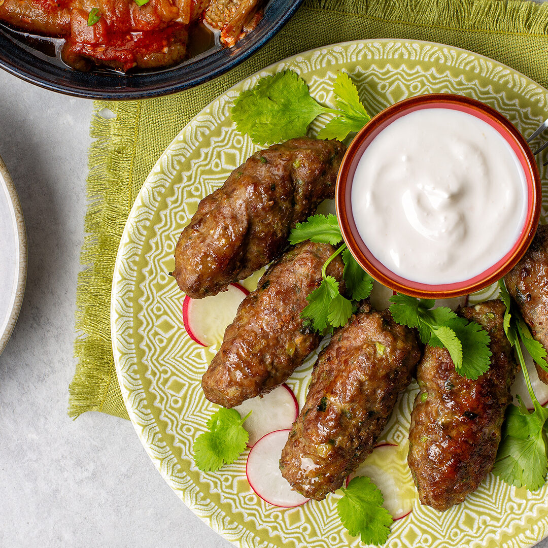 Beef koftas with yogurt, fresh coriander,  hummus and baked aubergines with tomatoes. Grey background. Vertical image.