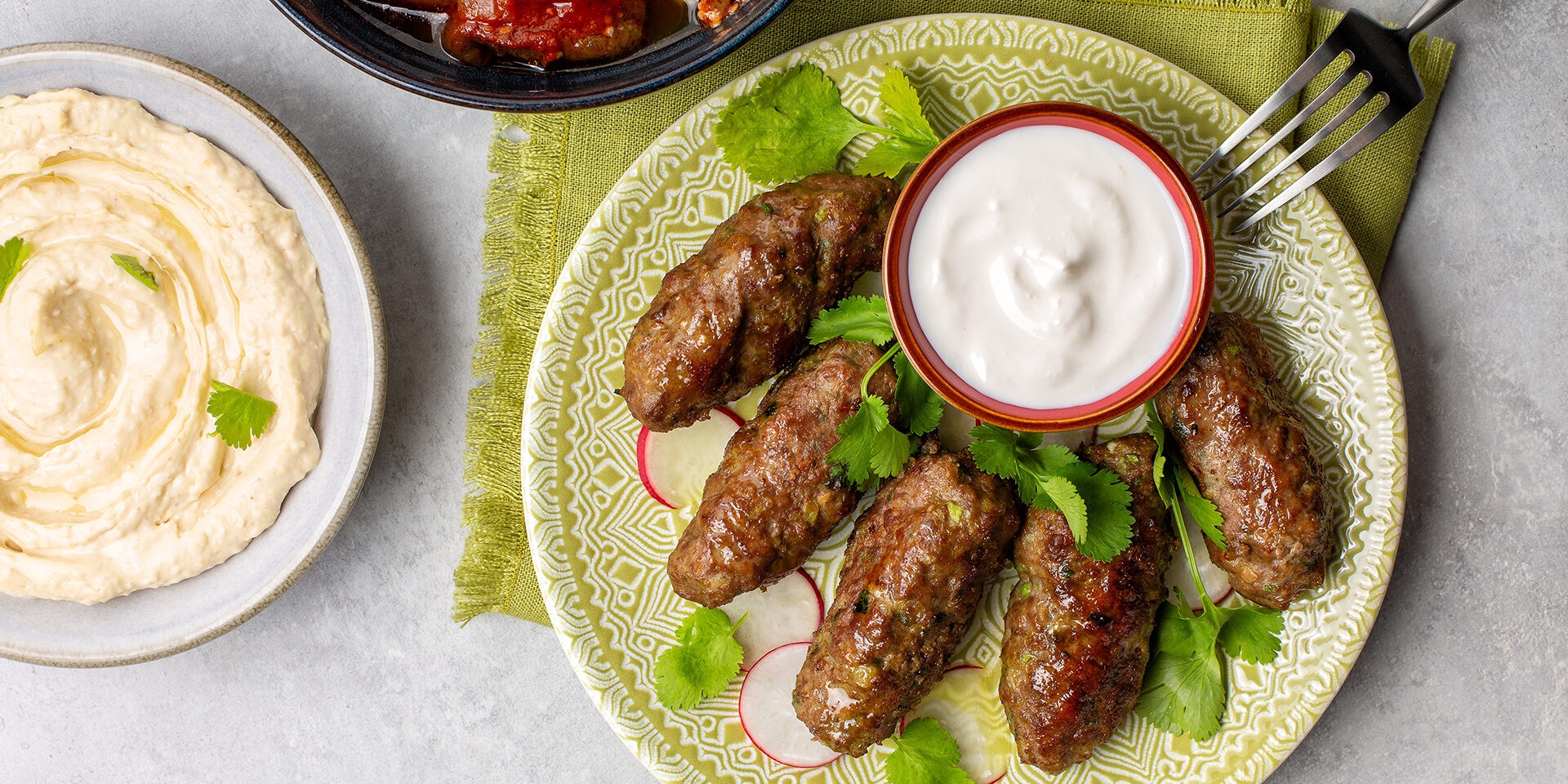 Beef koftas with yogurt, fresh coriander, hummus and baked aubergines with tomatoes. Grey background. Vertical image. Beef koftas with yogurt, fresh coriander, hummus and baked aubergines with tomatoes. Grey background. Vertical image.