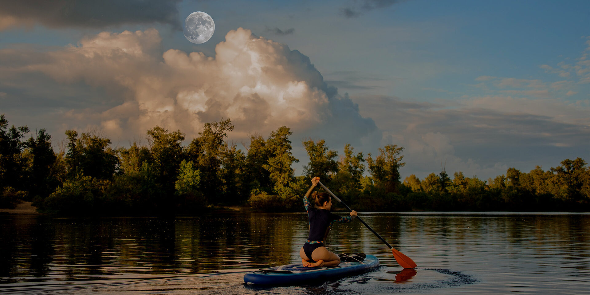 attractive young woman sits on sup board holds paddle in her hand and floats on the river
